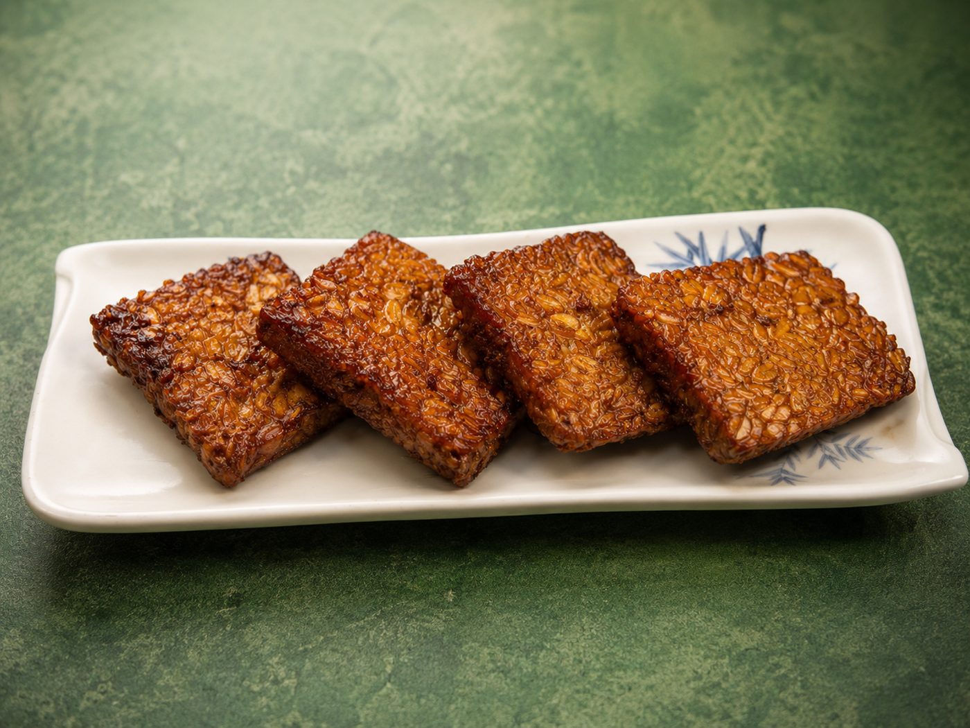 Caramelized tempeh slices on a ceramic plate — Indonesian restaurant food photography